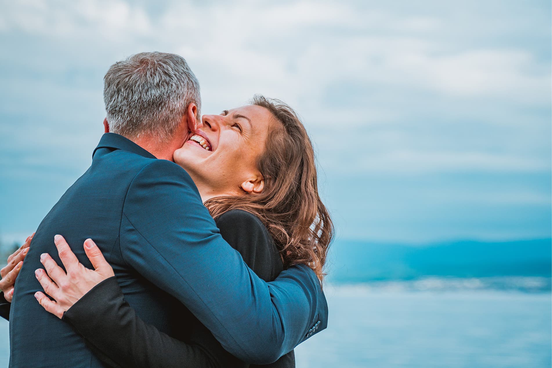 Endlich schuldenfrei umarmt sich ein erleichtertes Ehepaar am Strand mit der See im Hintergrund - Schuldnerberatung Hamburg Bergedorf